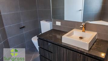 Un baño moderno con encimera de mármol oscuro, un lavabo blanco y un espejo grande.