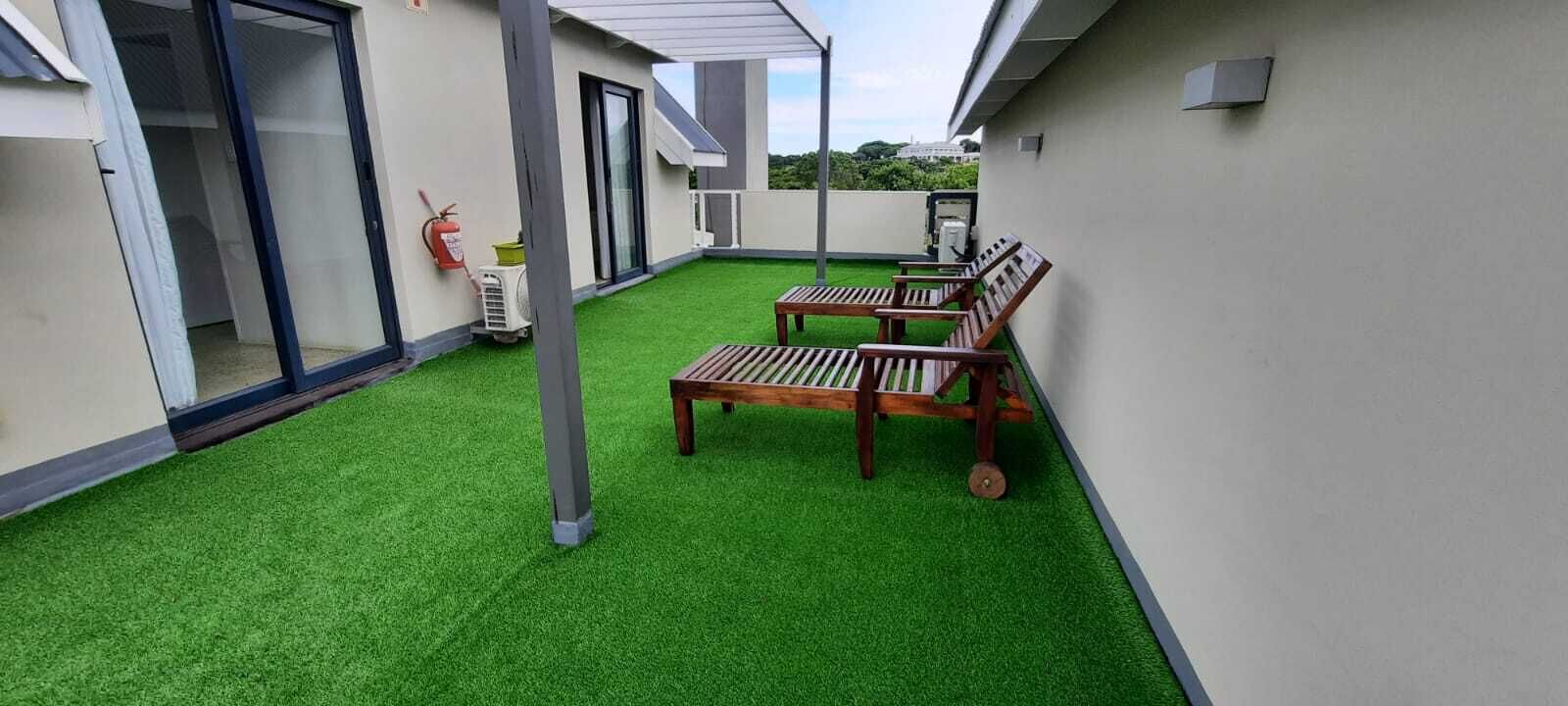 A rooftop terrace with artificial grass, wooden benches, and a fire extinguisher.