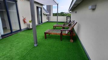 A rooftop terrace with artificial grass, wooden benches, and a fire extinguisher.