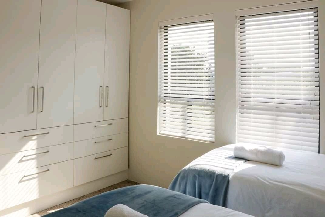 Une chambre à coucher avec un lit, une armoire et deux fenêtres équipées de stores.