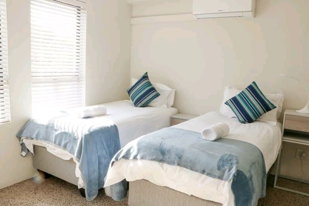 A room with two beds, each with a blue and white duvet, and striped pillows.