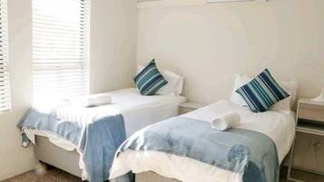 A room with two beds, each with a blue and white duvet, and striped pillows.