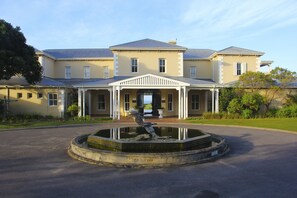 A large, two-story building with a symmetrical facade, a central entrance with a portico, and a circular water feature in the foreground.