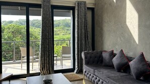 Una sala de estar moderna con un sofá gris, una mesita de centro y vistas al verde a través de ventanas amplias.