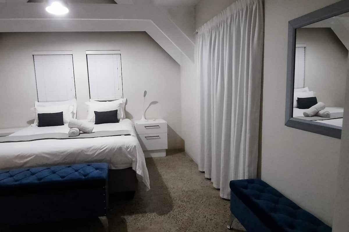 Une chambre à coucher avec un lit, des tables de chevet, un miroir et une fenêtre avec des rideaux.