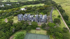 A modern multi-story hotel with a central courtyard, surrounded by lush greenery and a tennis court.