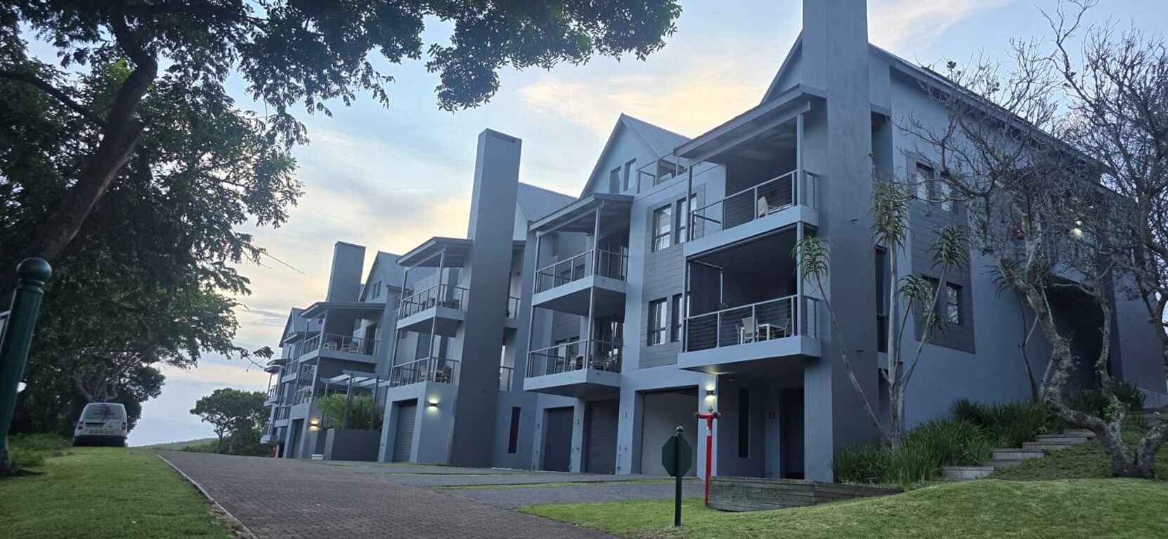 Un moderno edificio residenziale a più piani con balconi, vialetto d'accesso e cielo sereno.