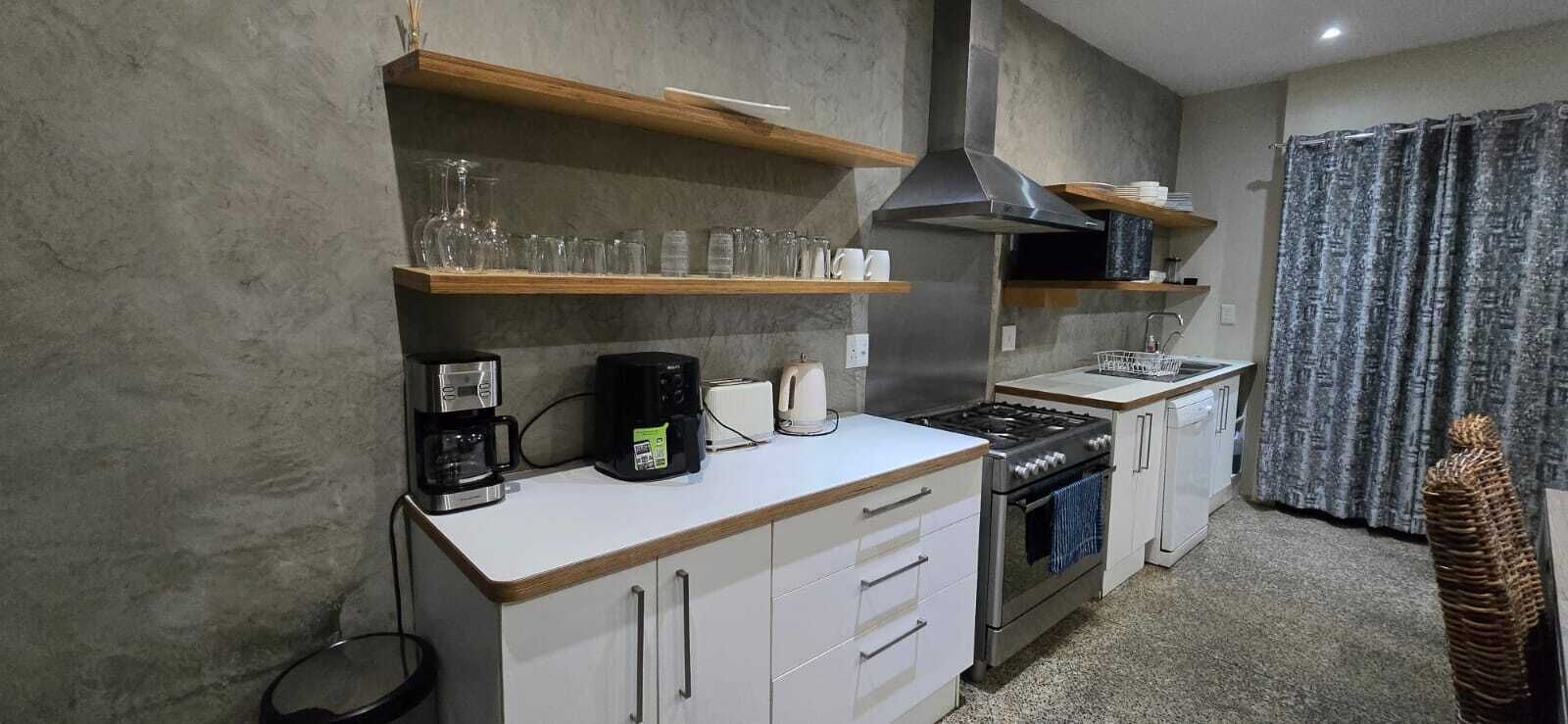 Une cuisine de taille réduite avec des meubles blancs, une cuisinière, une machine à café et de la vaisselle exposée sur des étagères.