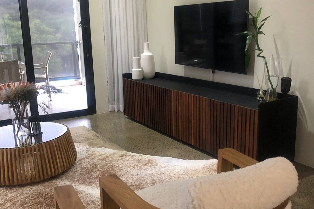 Un salon moderne doté d’un téléviseur à écran plat, de meubles en bois et d’une grande fenêtre offrant une vue sur la verdure.