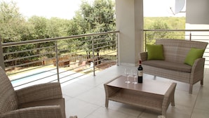 A balcony with wicker furniture, a pool, and a view of trees. - Tinyiko Kruger Lodge (Nkomazi)