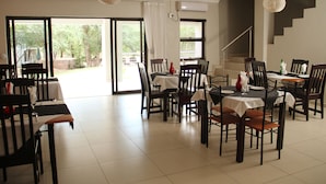 A dining area with multiple tables and chairs, a staircase, and a view of the outdoors. - Tinyiko Kruger Lodge (Nkomazi)