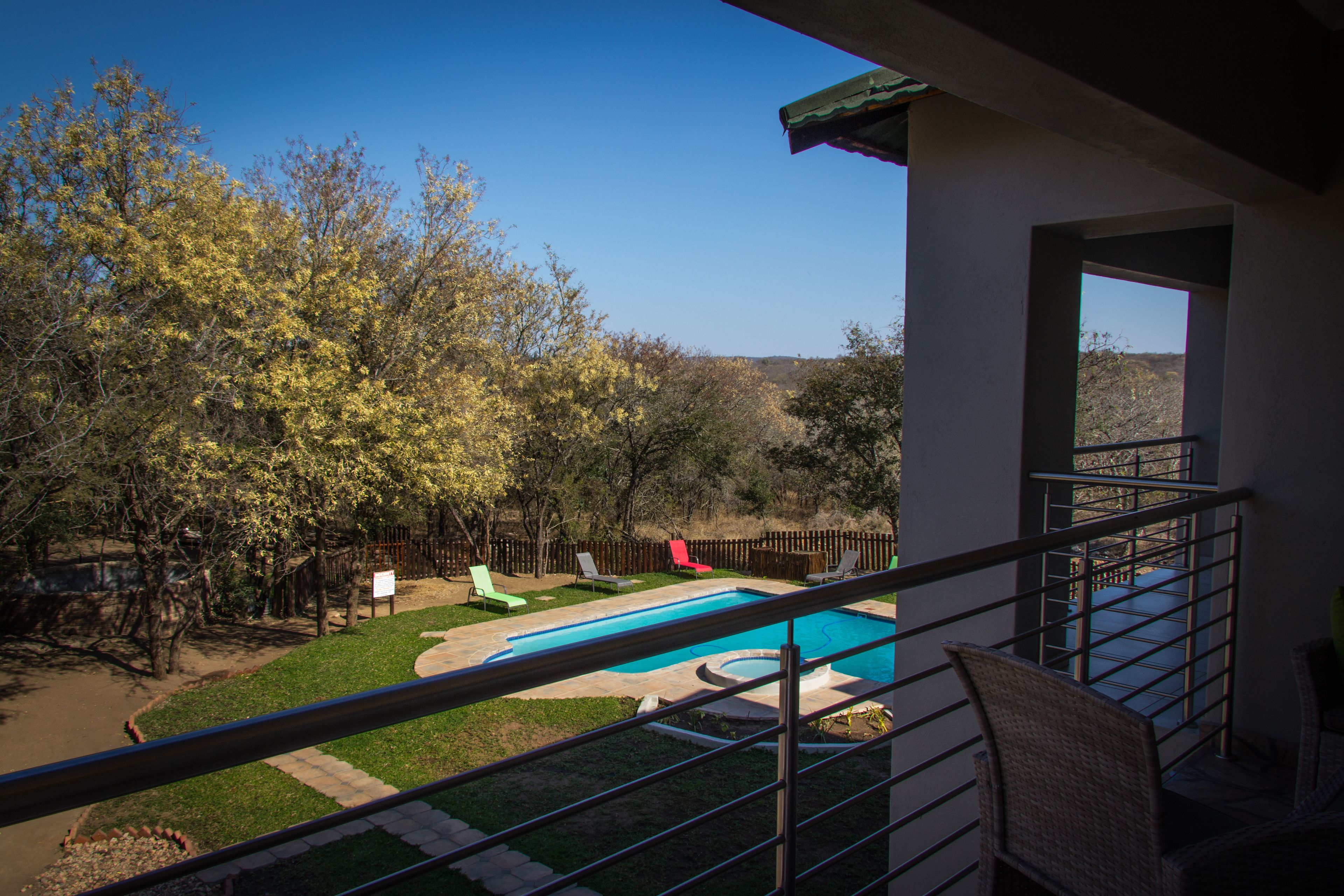 A backyard with a swimming pool, a fenced area, and a view of trees and hills.