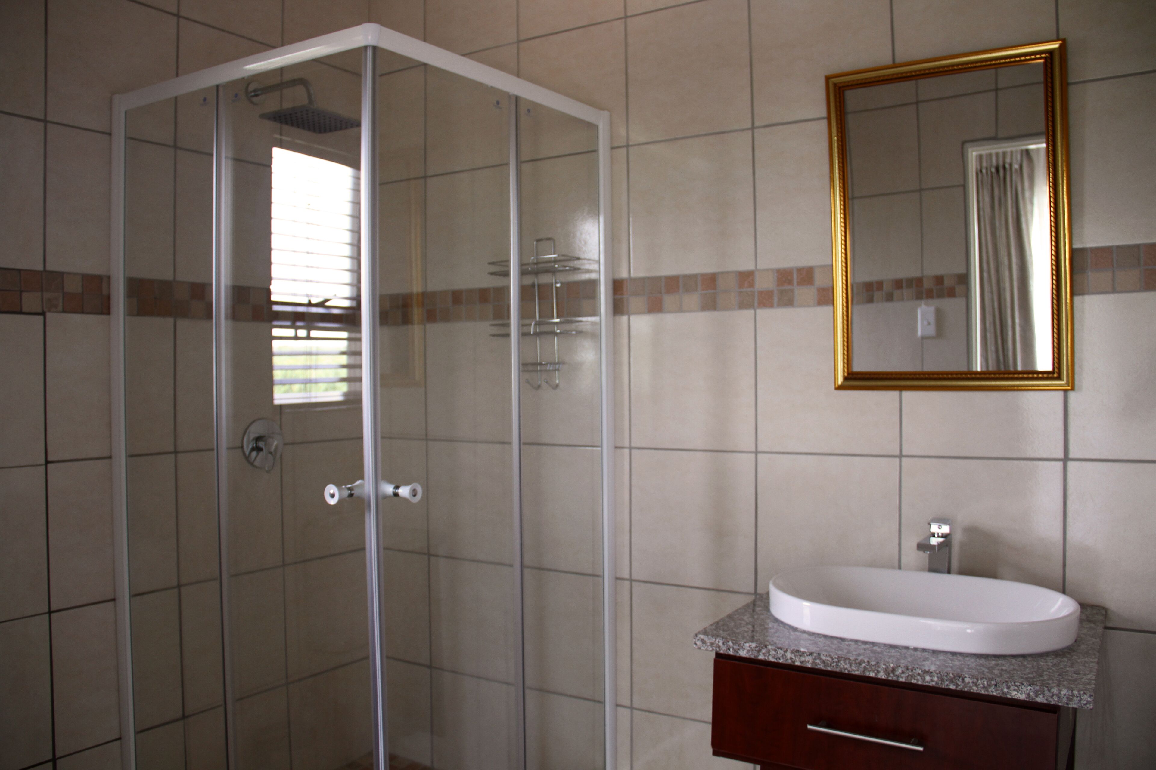 A bathroom with a glass-enclosed shower, a sink with a marble countertop, and a mirror with a gold frame.