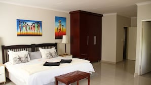 A hotel room with a large bed, a wooden bench, a wardrobe, and two paintings on the wall. - Tinyiko Kruger Lodge (Nkomazi)
