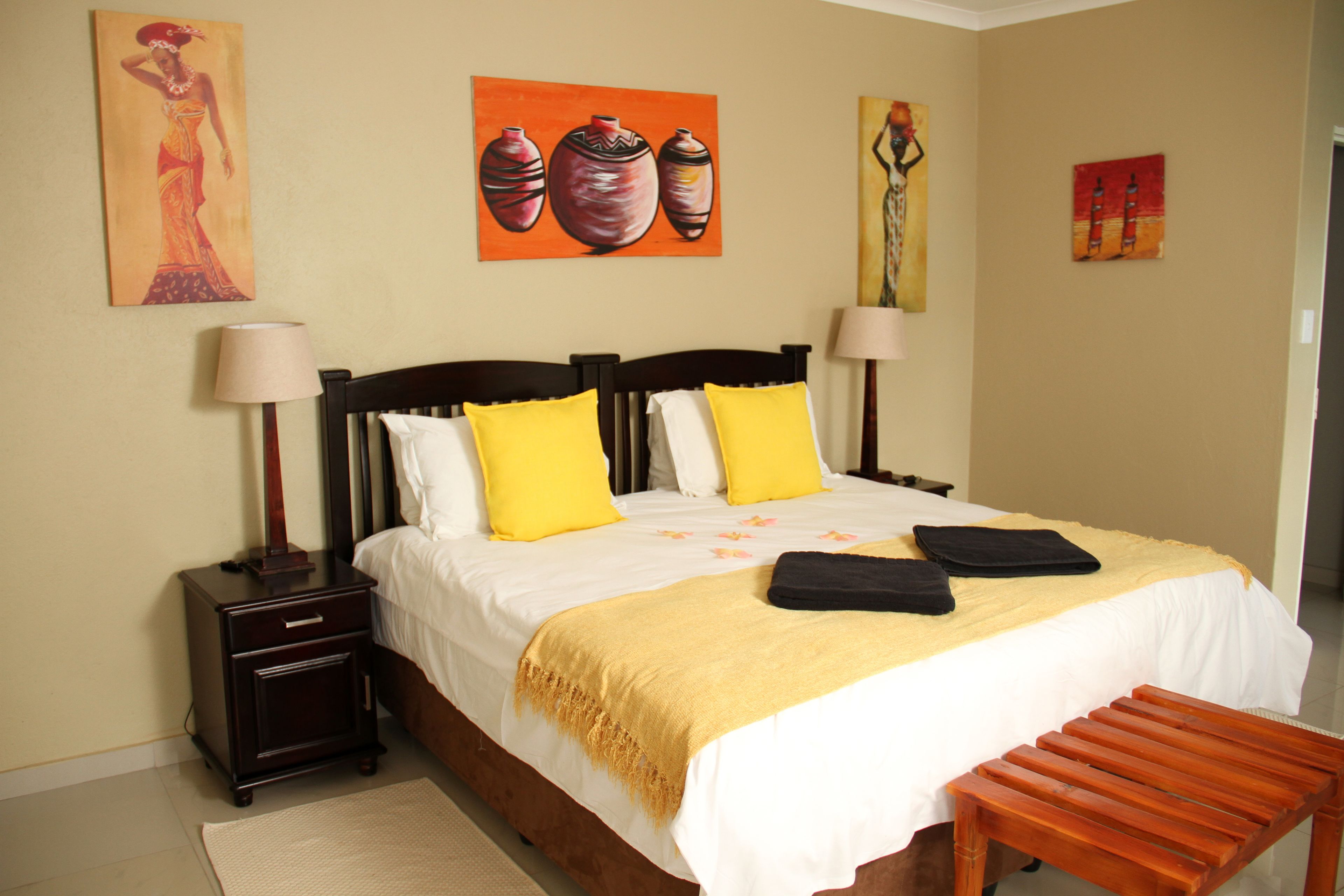 A neatly made bed with yellow and white pillows, a wooden bench, and artwork on the walls.
