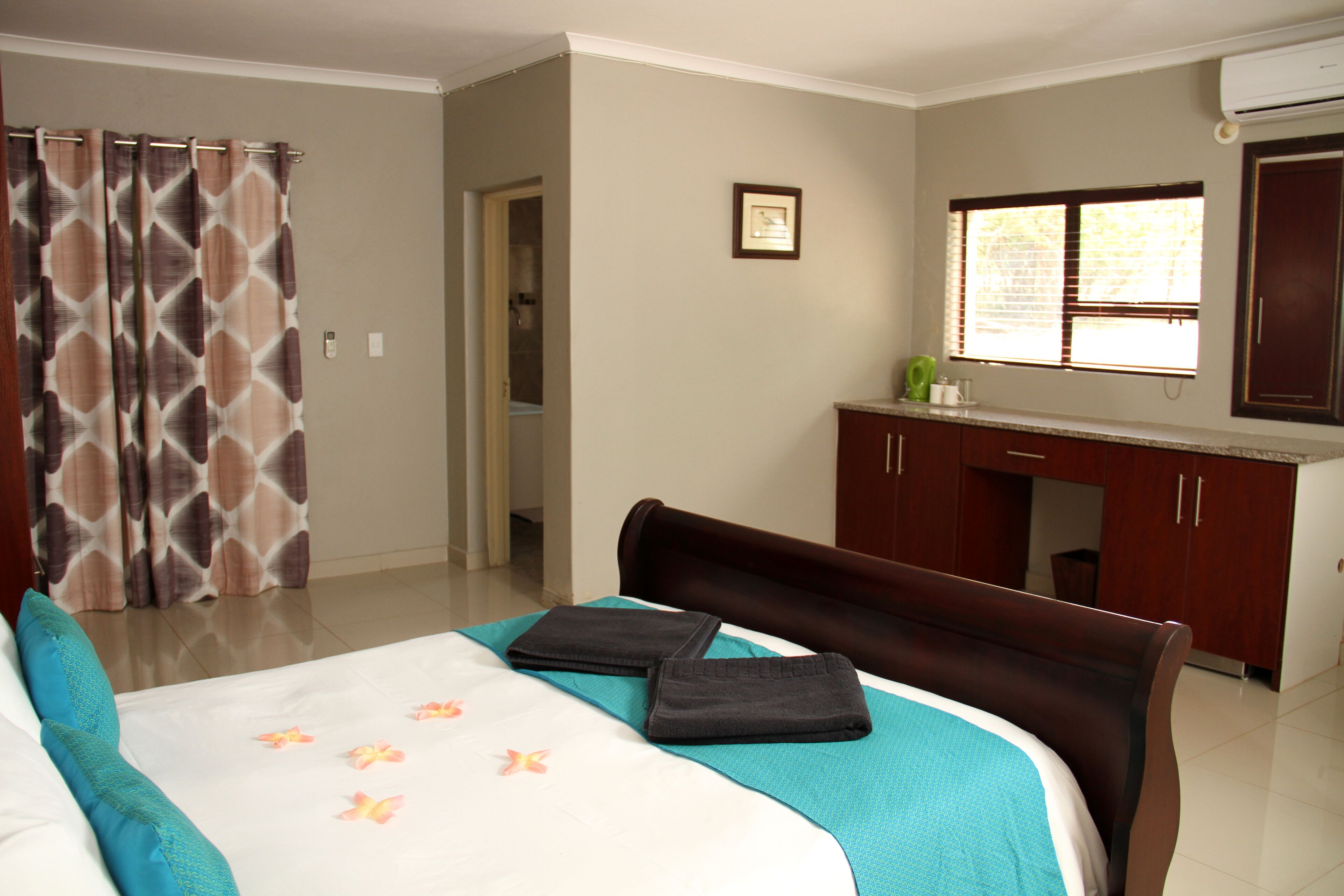 Une chambre d’hôtel comprenant un lit, une salle de bain, un coin cuisine et une fenêtre avec des stores.