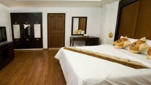 A bedroom with a wooden floor, a bed with white bedding, a wooden headboard, a small bedside table, and a mirror on the wall.