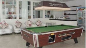 A pool table in a modern room with white sofas and a bar area.