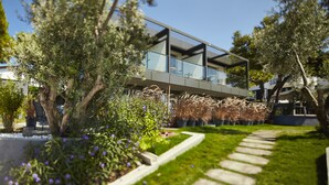 A modern house with a glass balcony, surrounded by well-maintained gardens and trees. - Kubana Hotel (Cesme)