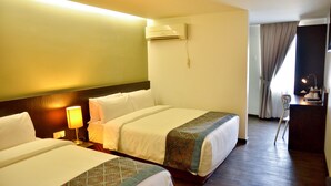 Habitación de hotel con dos camas, un escritorio con lámpara, aire acondicionado y vistas al exterior a través de una ventana con cortinas.