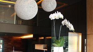 Un mostrador de recepción con un teléfono blanco, un pequeño jarrón blanco con orquídeas blancas y tres lámparas colgantes esféricas.