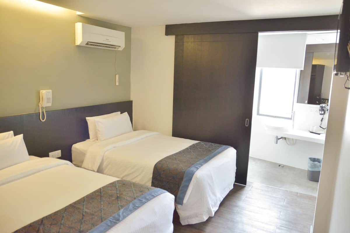 A hotel room with two beds, a bathroom with a sink and mirror, and an air conditioning unit on the wall.
