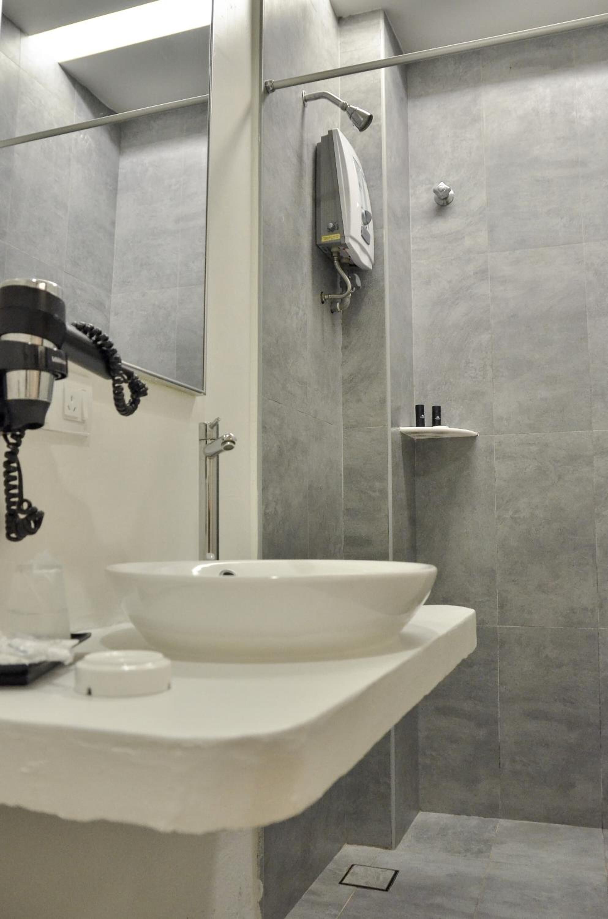 Un baño moderno con un lavamanos blanco, un cabezal de ducha de mano y un perchero para toallas.