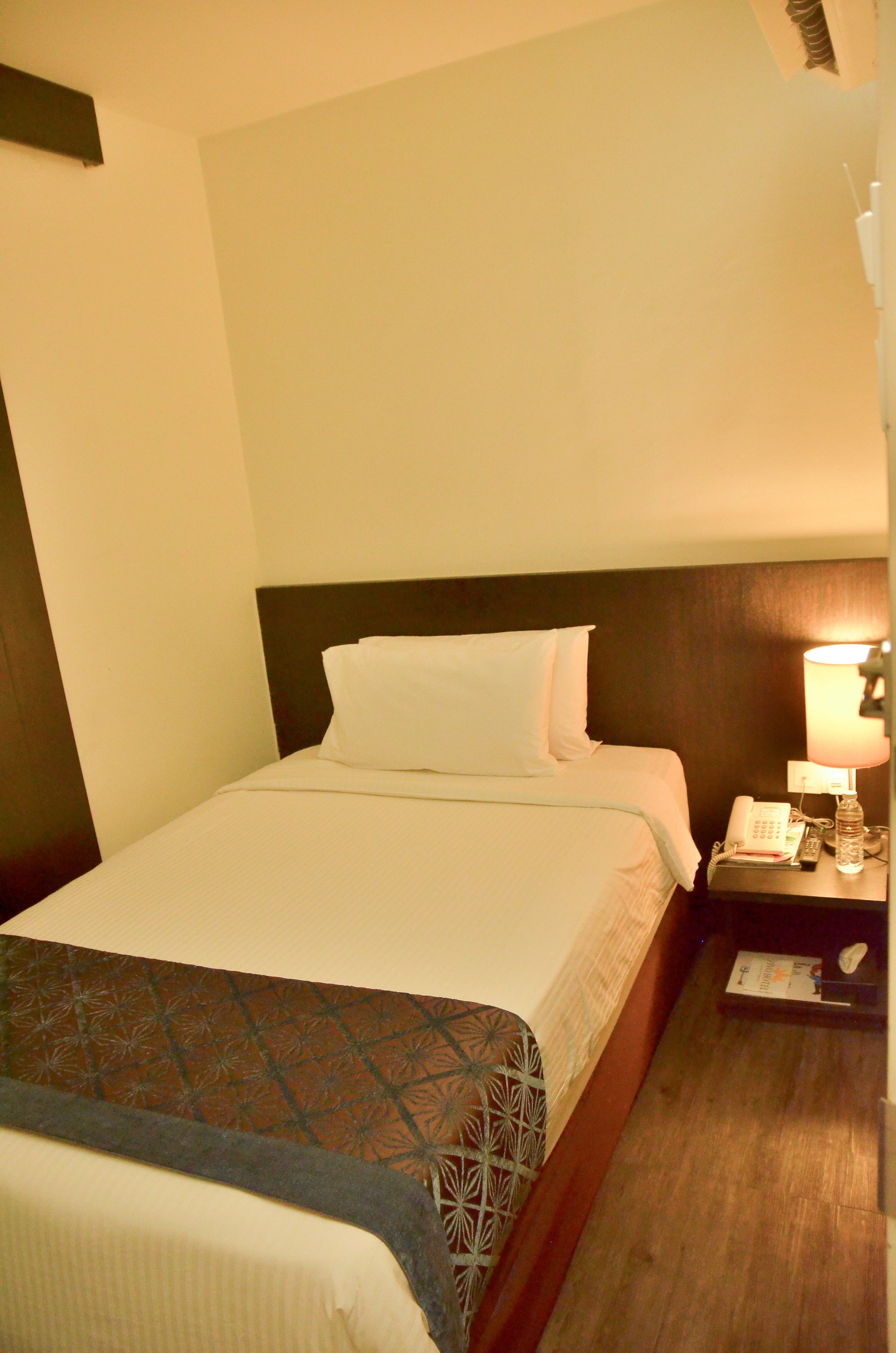 Una habitación de hotel con cama, mesita de noche con lámpara y teléfono.