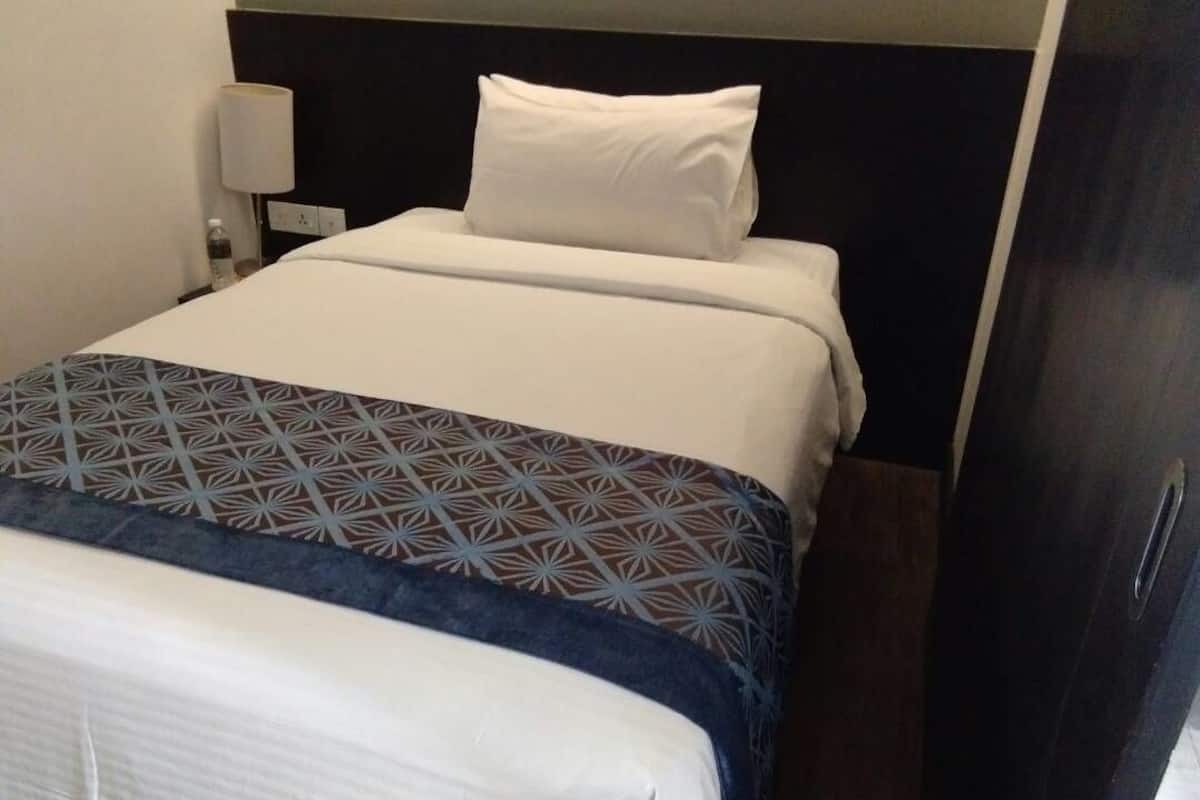 A hotel room with a bed, a bedside lamp, and a dark-colored door.