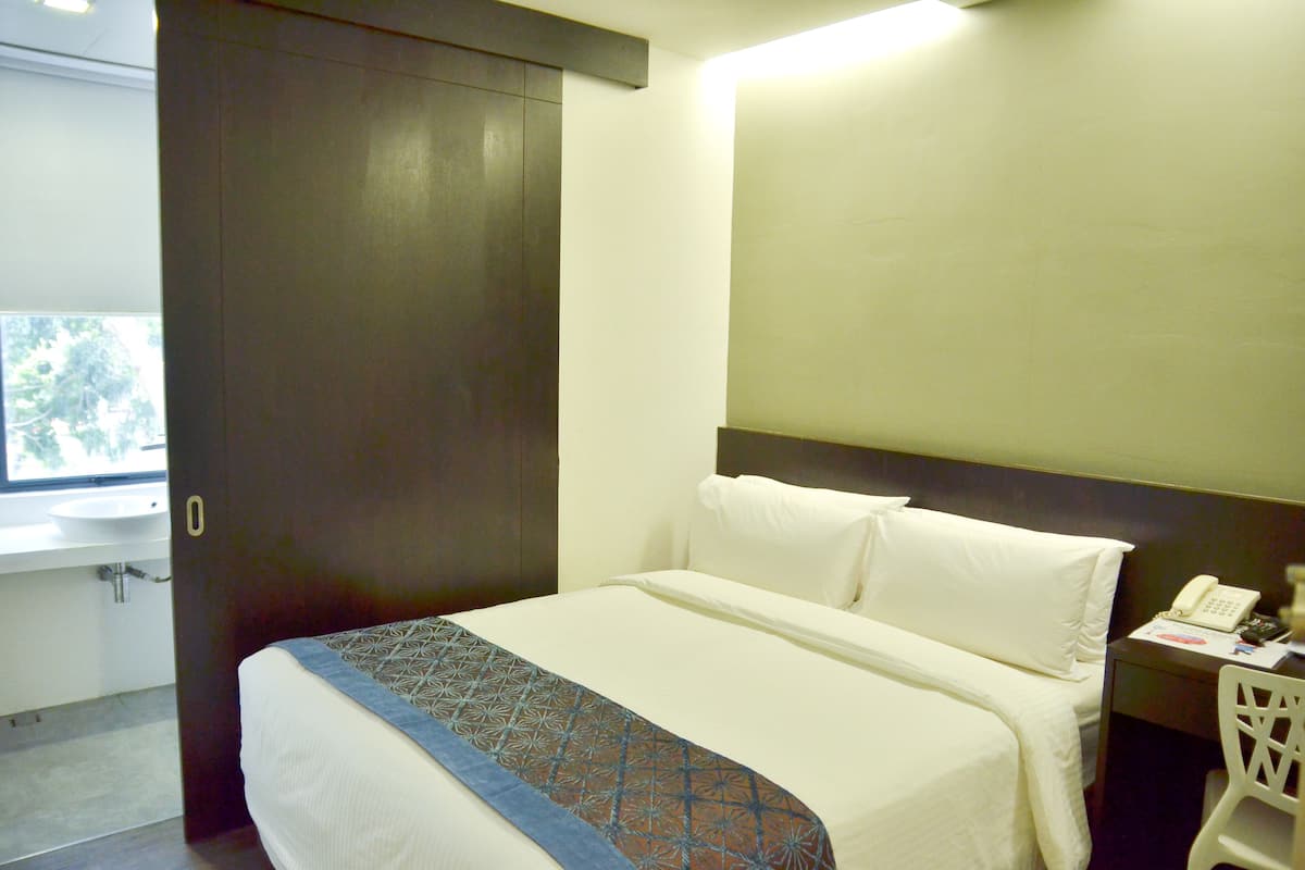 A hotel room with a bed, a bedside table with a phone, and a window with a view of trees.