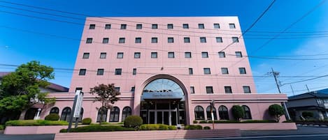 Un hotel rosa con una entrada central, varios pisos y un cielo despejado.