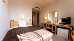 A hotel room with a large bed, a desk with a computer, a television, and a small refrigerator.