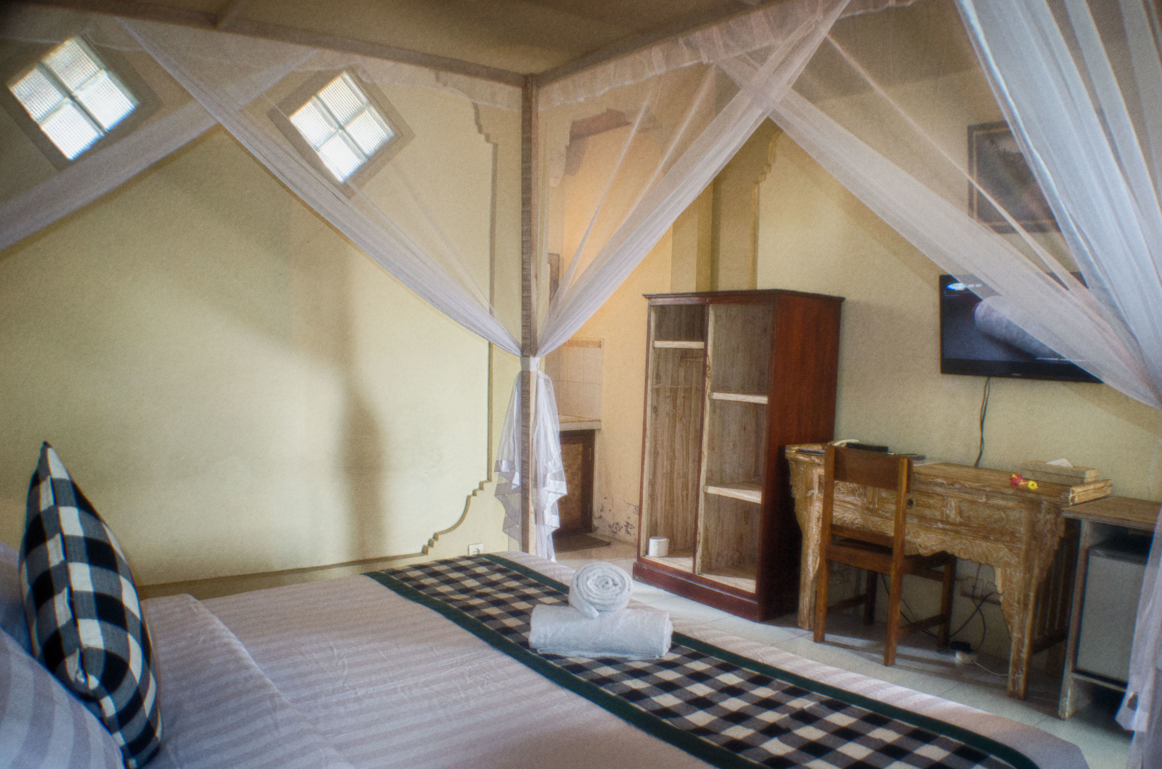 A bedroom with a bed, a wooden desk, a wardrobe, and a television.