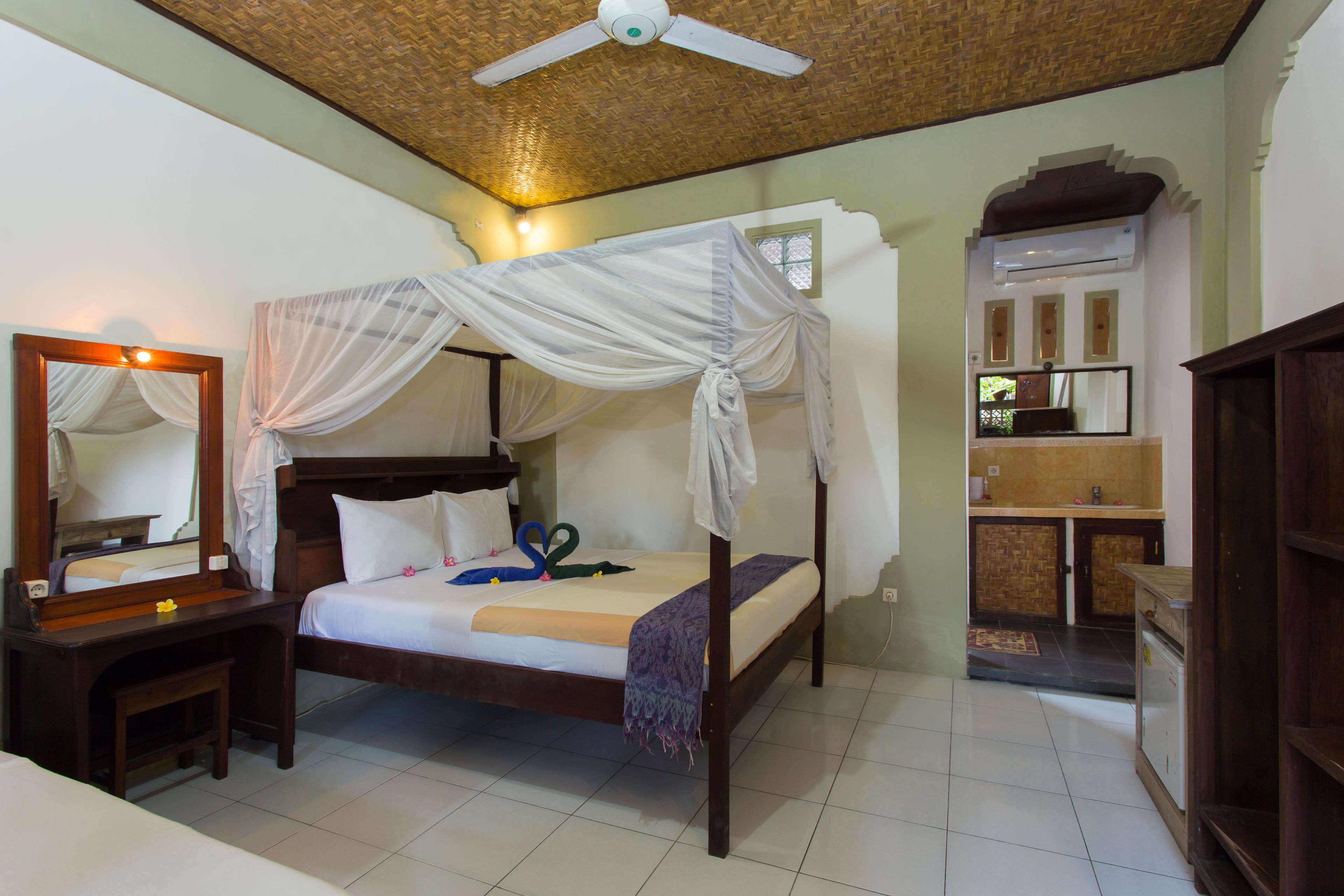 A bedroom with a four-poster bed, a wooden desk, a mirror, and a ceiling fan.