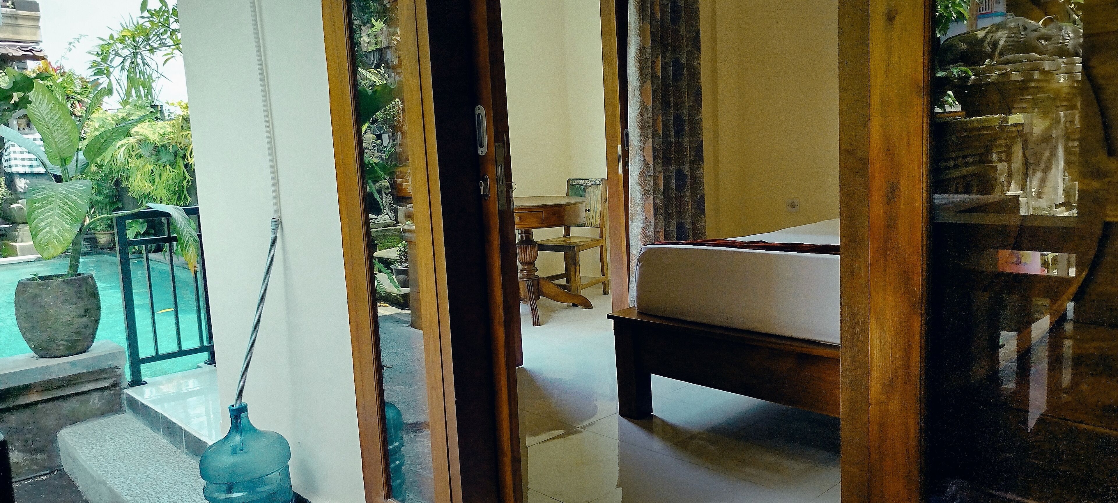A room with a bed, a small table, and a chair. There is a view of a pool and greenery outside.