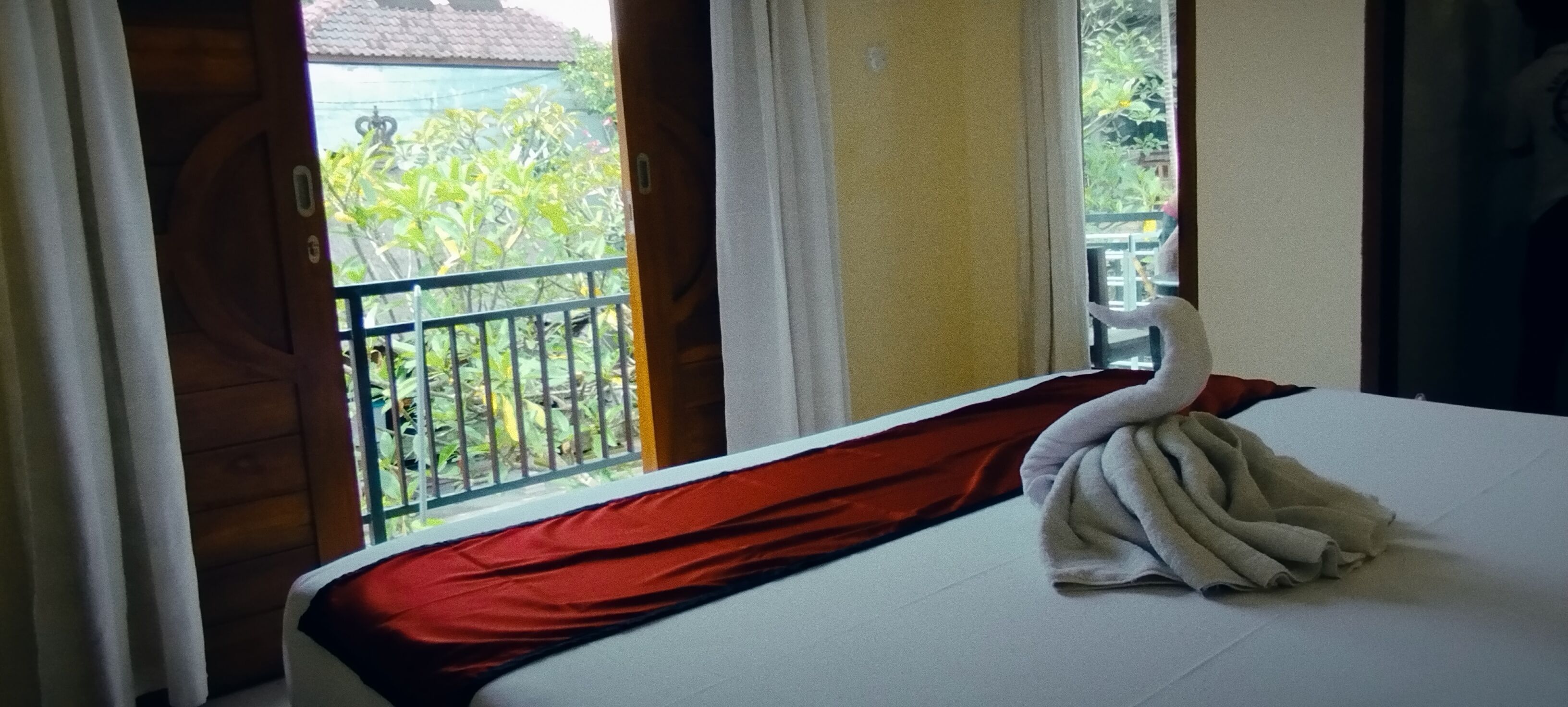 Ein Hotelzimmer mit Bett, einem Balkon mit Geländer und Blick auf die grüne Umgebung.