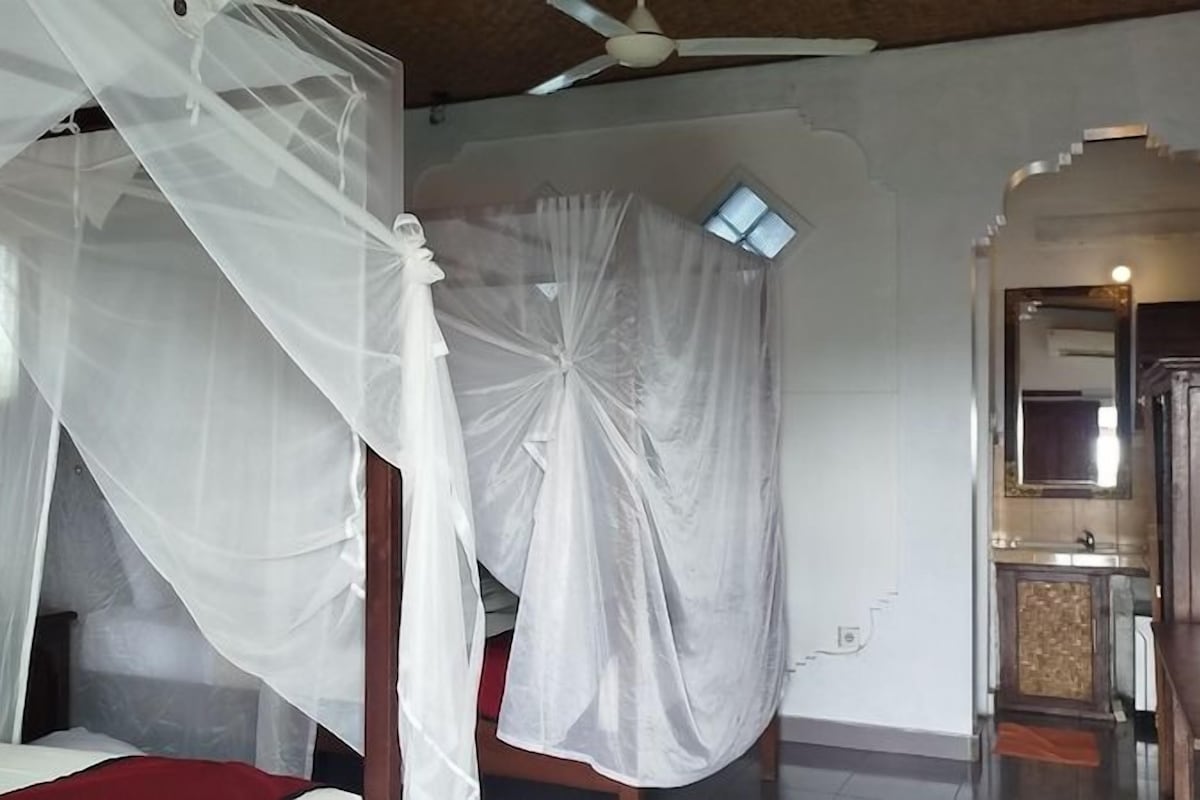 A room with a bed under a white canopy, a wooden cabinet, and a small window.