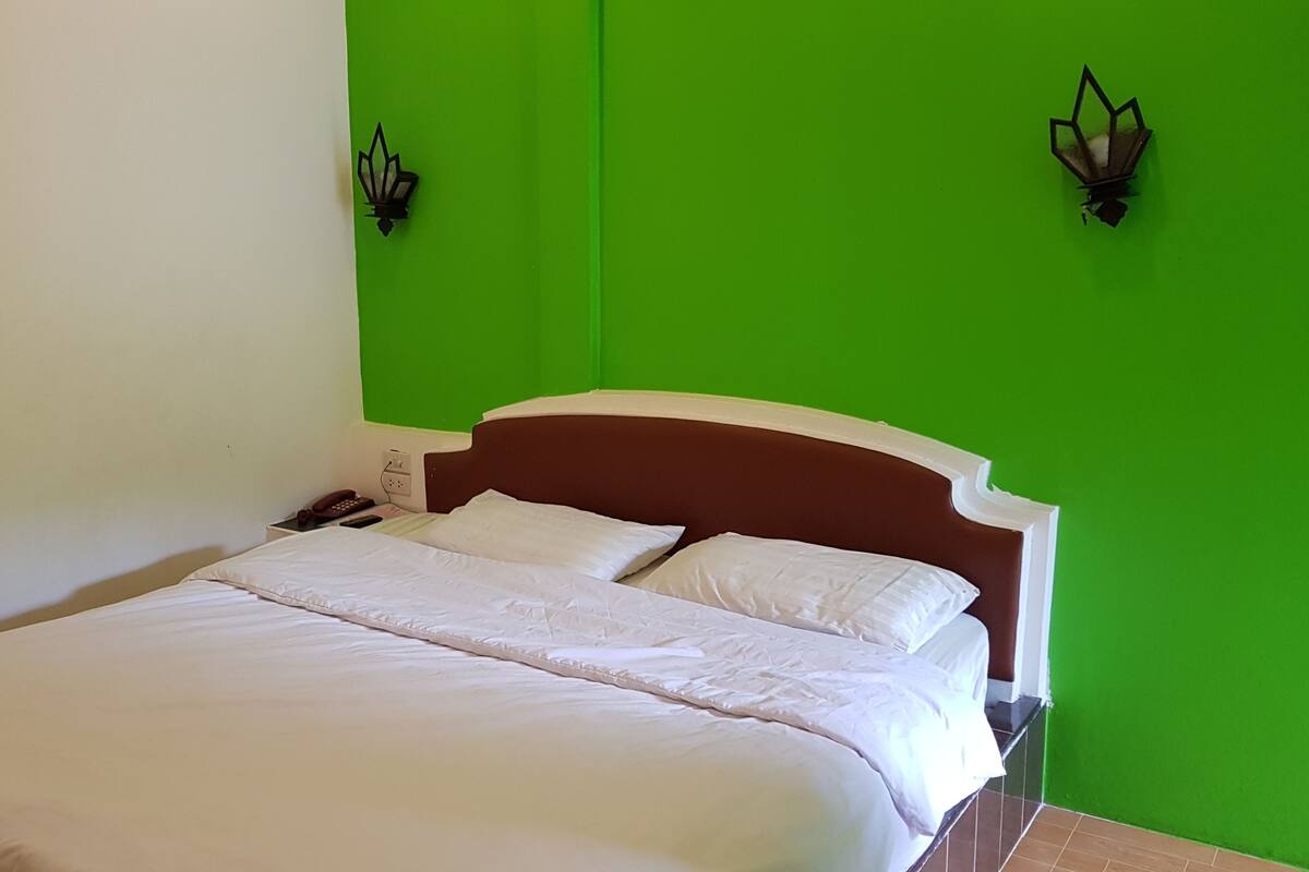 A bed with white bedding in a room with green walls and a brown headboard.