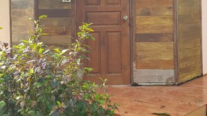 Une porte en bois avec une enseigne au-dessus, un petit porche et une plante au premier plan.