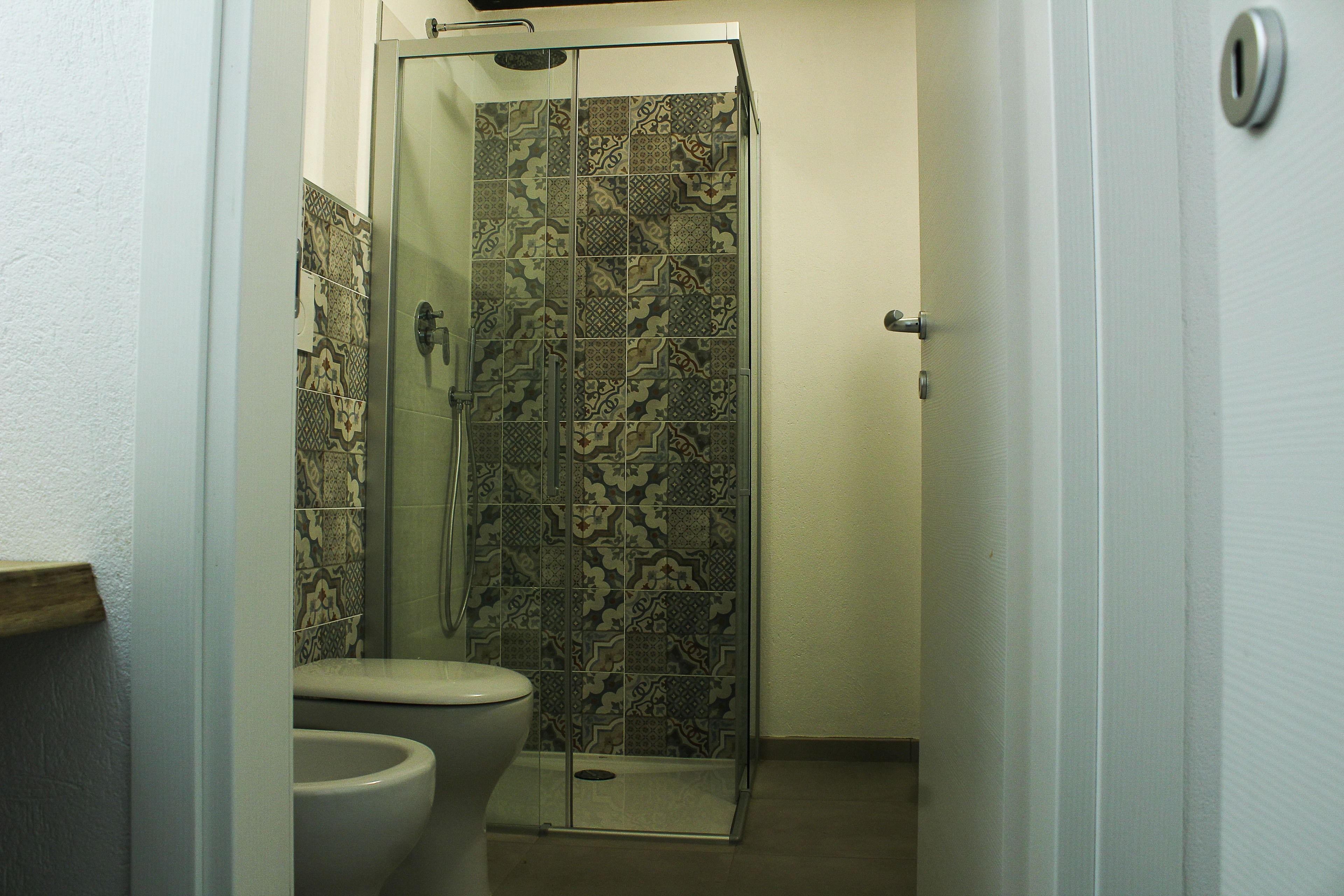 A bathroom with a shower, toilet, and patterned tiles.
