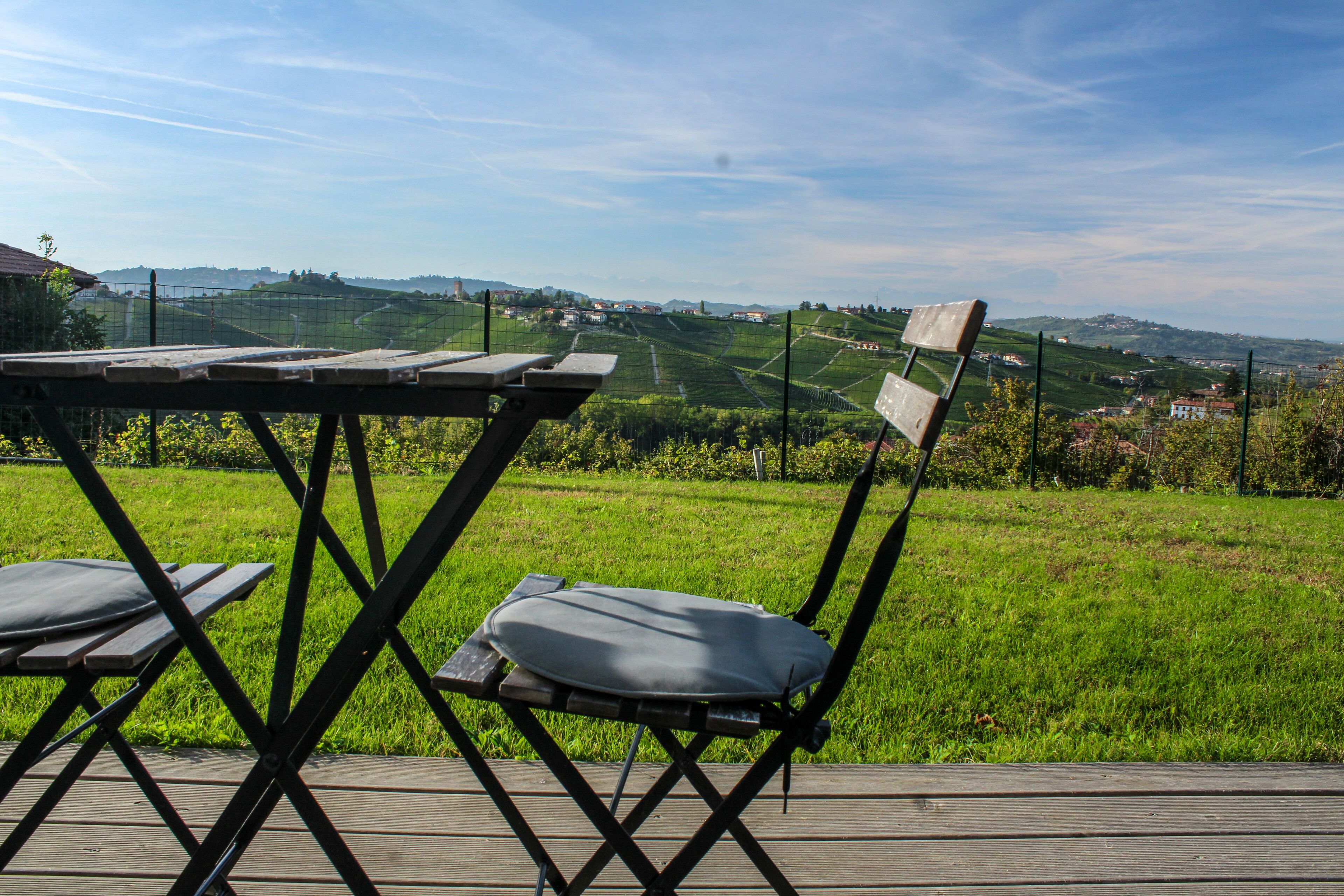 Una terraza de madera con una mesa y sillas, con vistas a un paisaje verde con colinas y una valla.