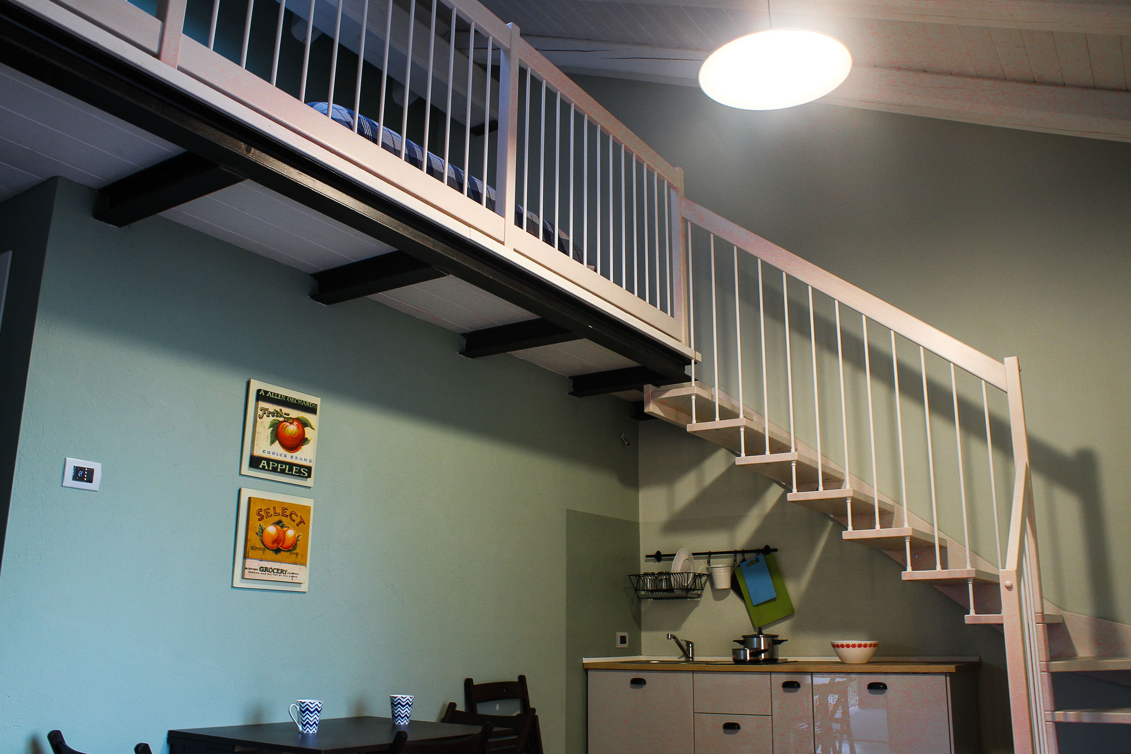 A kitchen with a wooden staircase, a dining table with chairs, and a hanging light fixture.
