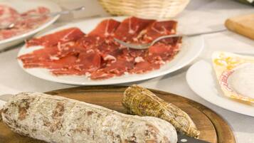 Un tavolo con diversi cibi tra cui affettati, una grossa salsiccia e un involucro, forse formaggio o pasta.