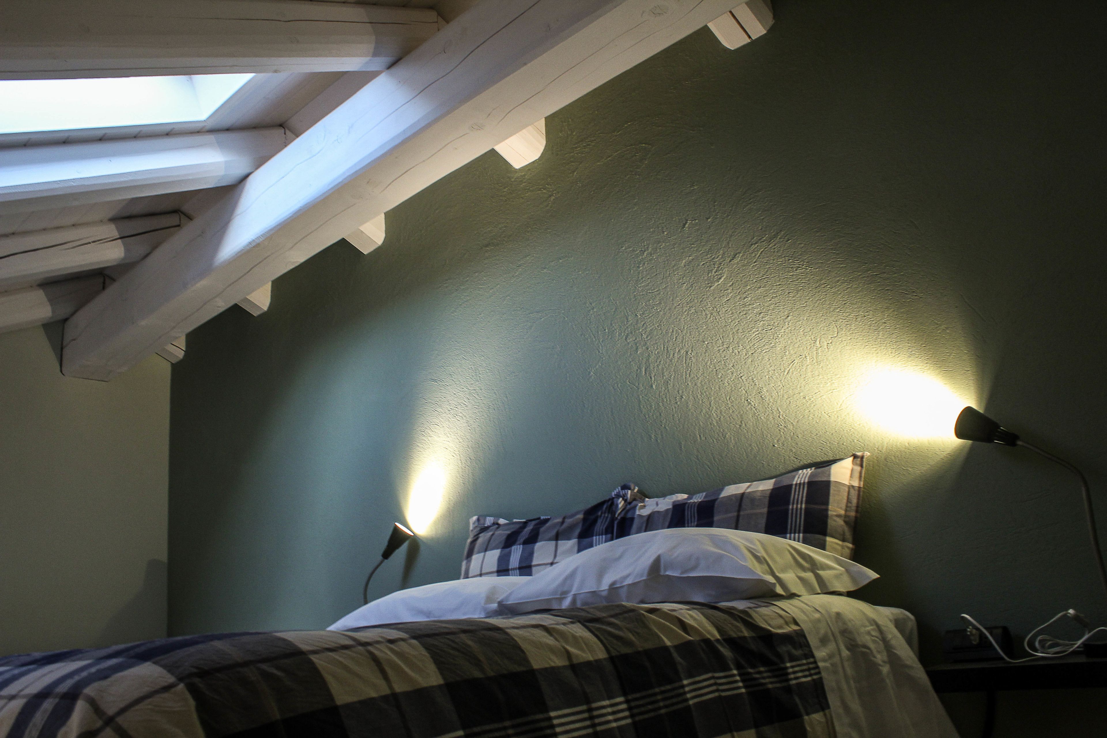 A room with a bed, a skylight, and a wall-mounted lamp.