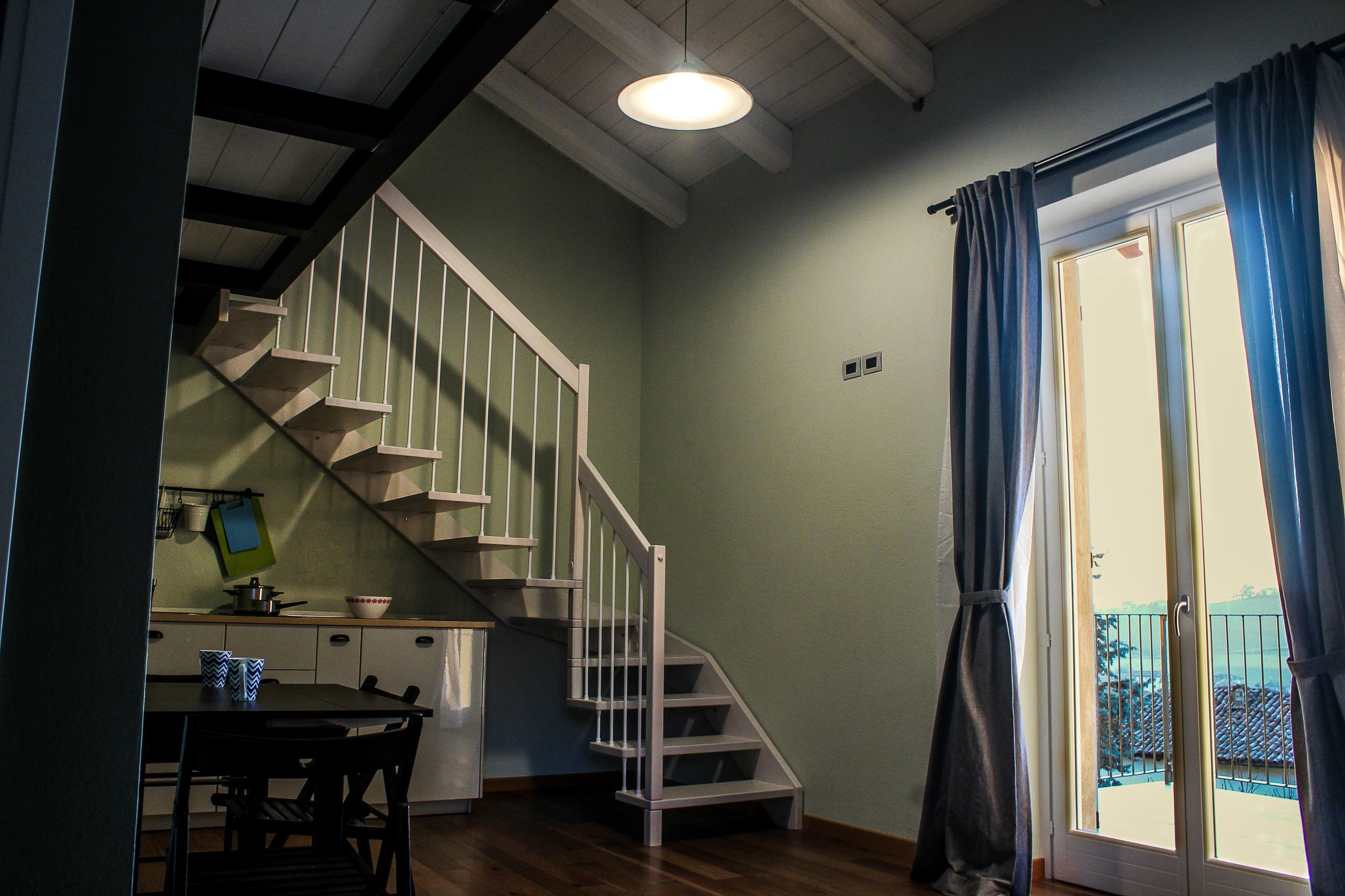 A staircase leading to a balcony with a view, a dining area with a table and chairs, and a kitchen area with cabinets and a sink.
