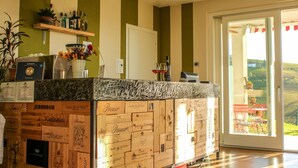 A bar area with wooden crates as a countertop, a shelf with bottles, and a view of the outdoors through a glass door. - Ca dei Currà (Neive)