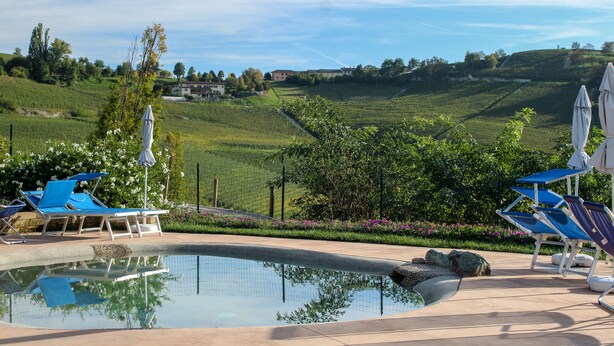 A pool area with lounge chairs and umbrellas, surrounded by a landscaped garden and a view of rolling hills. - Ca dei Currà (Neive)