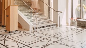 Un interior moderno con piso de estampado geométrico, una escalera con barandillas de metal y un ventanal con vistas.