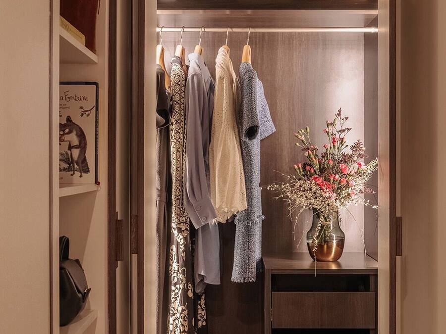 A walk-in closet with hanging clothes, a handbag, and a vase with flowers.