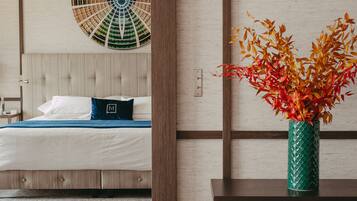 Una habitación de hotel con una cama, una mesita de noche con un florero y un ventilador de pared.